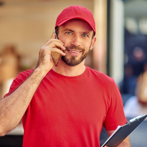 young-cheerful-caucasian-male-courier-in-red-uniform-talking-on-phone.jpg